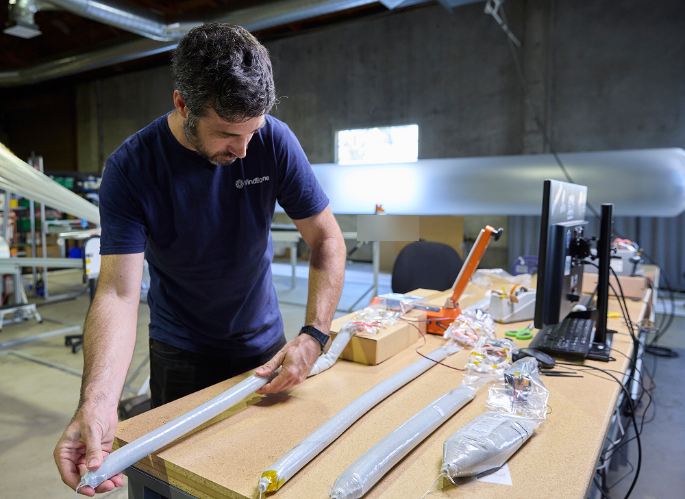 A WindBorne engineer measures a long ballast component at a workshop table.