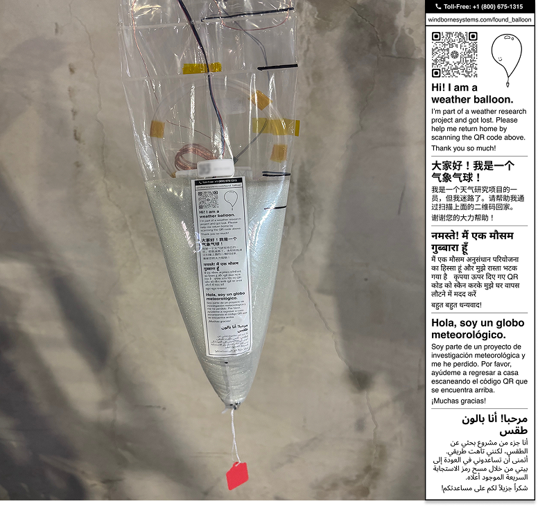 A weather balloon carries a printed recovery label and red sticker.